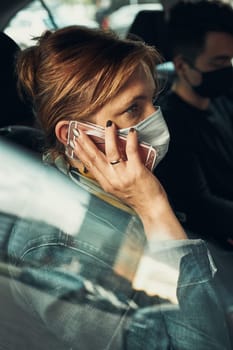 Woman talking on phone using smartphone sitting in a car wearing the face mask to avoid virus infection and to prevent the spread of disease in time of coronavirus