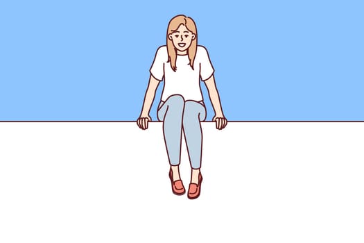 Young woman sits on blank billboard designed to advertise or promote marketing campaign. Positive student girl sits with legs dangling on large billboard calling for attention to advertisement