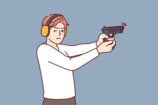 Man with gun trains at shooting range to learn how to shoot and become sheriff or bodyguard. Guy in ballistic headphones holds gun and squints to hit target during training in shooting range