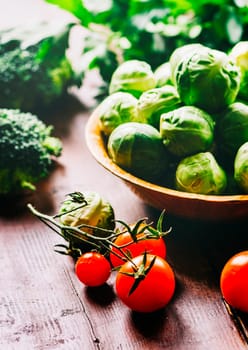 Brussel sprout, cherry tomato, broccoli, parsley and greens on rustic wooden table. Superfood vegetable salad mix on vintage background. Closeup of healthy food ingredients still life. Organic and vegan recipe cuisine concept.