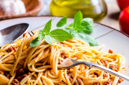 Closeup of italian spaghetti bolognese with basil in fork. Traditional homemade mediterranean food recipe. Italian pasta with tomato, meat, basil and olive oil served in plate.