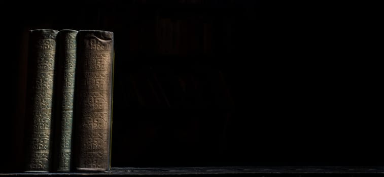 Old book on wooden bookshelf over black background. Vintage book covers still life on dark backdrop. University education study.