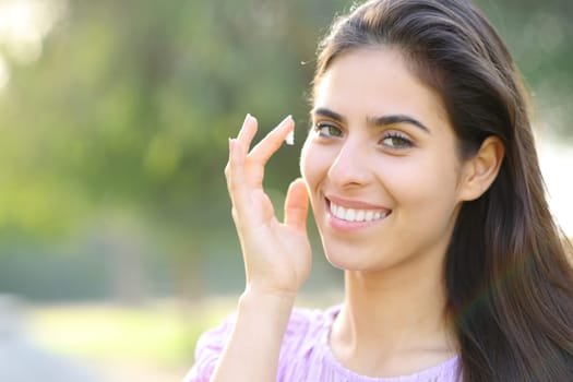 Beauty happy woman hydrating face skin with cream in a park