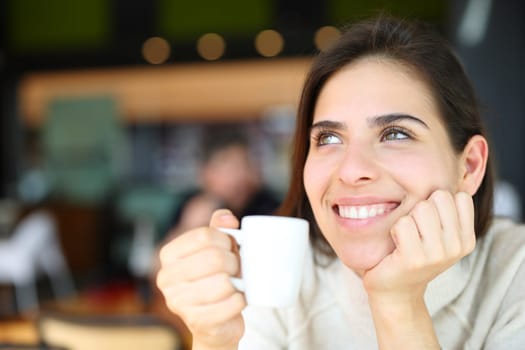Happy woman dreaming drinking coffee in a restaurant