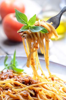 Closeup of italian spaghetti bolognese with basil in fork. Traditional homemade mediterranean food recipe. Italian pasta with tomato, meat, basil and olive oil served in plate.