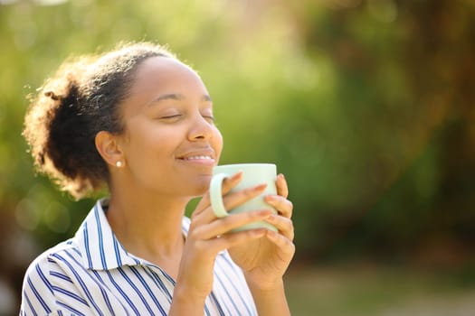 Relaxed black woman smelling coffee cup resting in a park