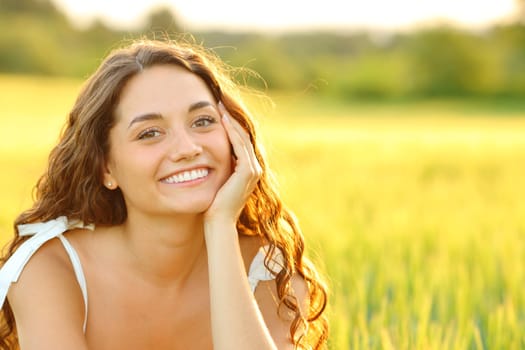 Happy woman with beauty smile posing at sunset in a wheat field