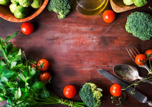 Top view of healthy food ingredients frame on vintage wooden table. Superfood vegetable mix border on rustic background from above. Cherry tomato, sprout brussels, broccoli, parsley, greens and olive oil overhead.
