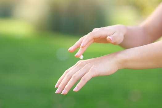Close up of a woman hands hydrating skin with cream in a park