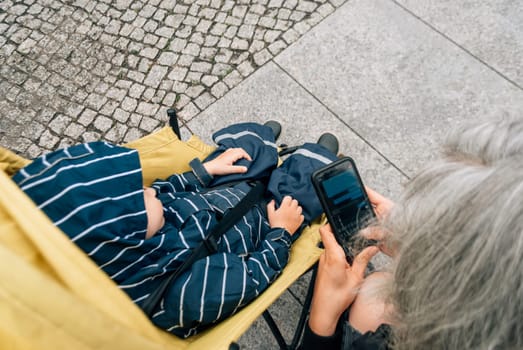 Top view of a woman typing a message on her phone, near a stroller with a child.