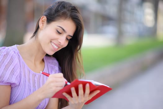 Happy female writing in paper agenda sitting in the street