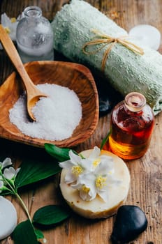 Natural spa cosmetics with essential massage oils, jasmine flower petals, zen stone on rustic wooden background. Handmade soap and herbal aromatherapy wellness treatment. Luxury skincare salon.