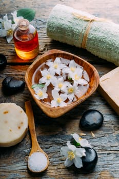 Natural spa cosmetics with essential massage oils, jasmine flower petals, zen stone on rustic wooden background. Handmade soap and herbal aromatherapy wellness treatment. Luxury skincare salon.