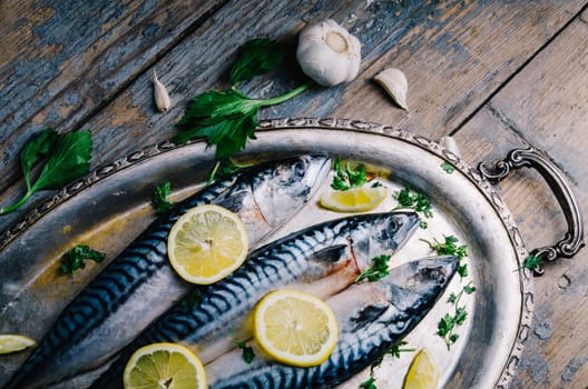 Fresh mackerel fish with lemon and spices served on silver plate from above. Homemade seafood dish recipe cooking. Healthy diet food prepared for dinner.