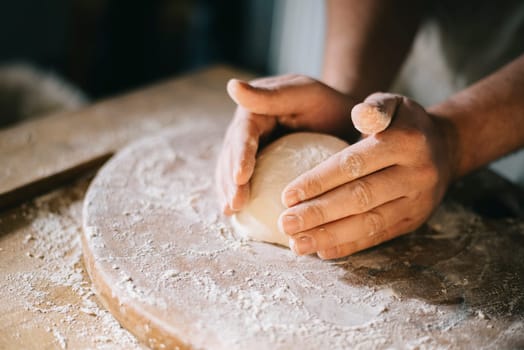 Man kneading and baking homemade pizza dough in the kitchen. Closeup on baker's hands preparing loaf of bread. Cooking and food preparation at home.