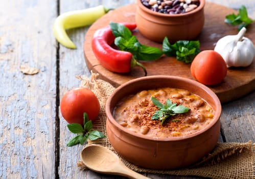 Traditional baked beans in tomato sauce cooked in retro clay pot with spices and vegetables. Homemade healthy cuisine.