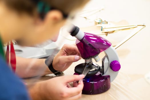 Boy looking through a purple microscope at a bird feather, at a children's science event