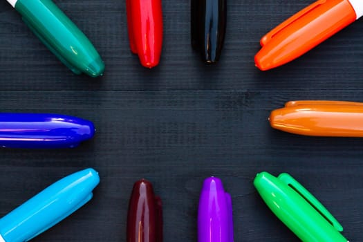Multi-colored markers on a black wooden background. Top view. Copy space