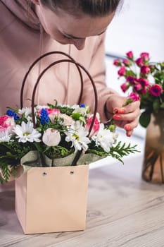 Female picking up bouquet of different flowers in paper gift bag with handles, vertical