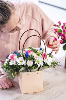 Female picking up bouquet of different flowers in paper gift bag with handles, vertical