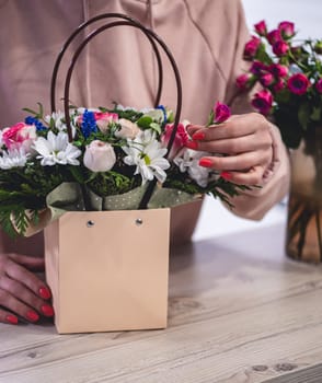 Female picking up bouquet of different flowers in paper gift bag with handles, vertical