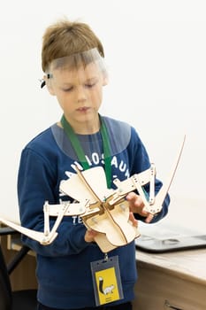 Boy wearing a protective screen with a movable wooden mock-up of a bird skeleton at a children's science event during the coronavirus pandemic