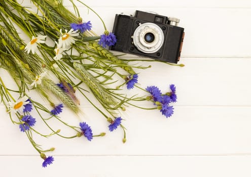Retro vintage old camera with cornflowers and daisies on a white wooden background. Top view. Copy space.