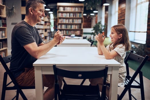 Father playing rock, paper, scissors game with her daughter in public library. Little girl spending time with dad. Positive competition. Family bonding