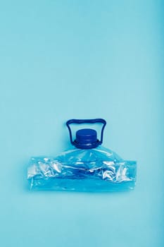Squashed empty plastic bottle over blue background. Collecting plastic waste to recycling. Concept of plastic pollution and too many plastic waste. Copy space at the top