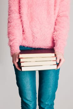 Young girl holding a few books. Teenager girl wearing pink sweater and blue jeans. Vertical photo