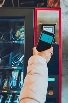 Woman paying for product at vending machine using contactless method of payment with mobile phone. Woman using new way of payments