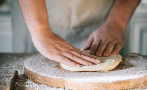 Man kneading and baking homemade pizza dough in the kitchen. Closeup on baker's hands preparing loaf of bread. Cooking and food preparation at home.