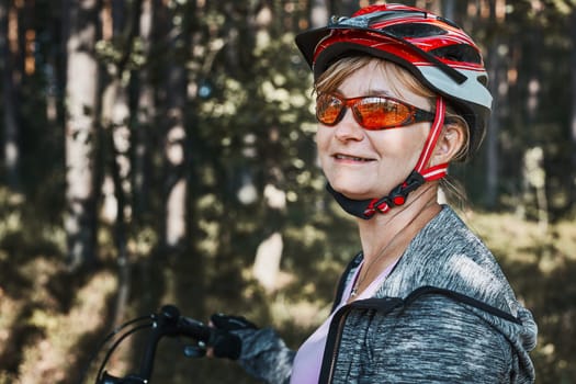 Active woman cycling on forest road. Female riding bicycle off-road route on summer vacation day. Woman wearing bicycle helmet and gloves