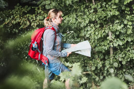 Woman with backpack having break during trip in mountains looking at map sitting on grass on summer vacation day