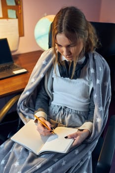 Student learning remotely from home. Young woman having classes online, making notes, reading and learning sitting at desk at home during quarantine