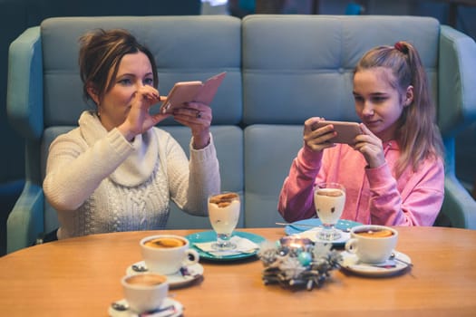 Women taking photos of dessert in coffee shop, using smartphone camera. Candid people, real moments, authentic situations