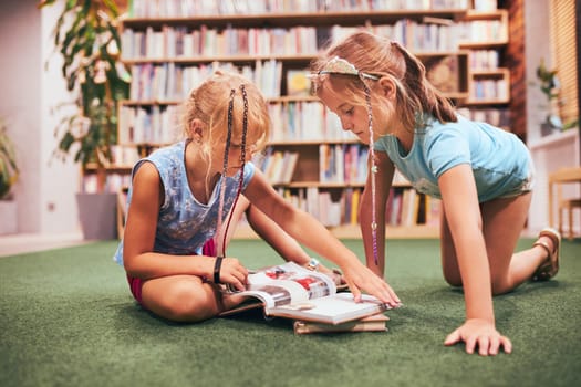 Two schoolgirls reading books in school library. Primary school students learning from books. Pupils doing homework. Children having fun with books in school club. Back to school