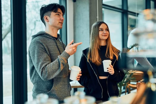 Friends doing shopping in a coffee shop. Young man and woman having chat while picking out the pastry, bakery's goods and hot drinks standing at counter in a coffee shop. People buying coffee and sweet snacks to go