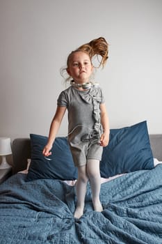 Little girl singing holding headphones cord imitating herself a real singer. Child having fun jumping dancing listening to music on bed in bedroom at home