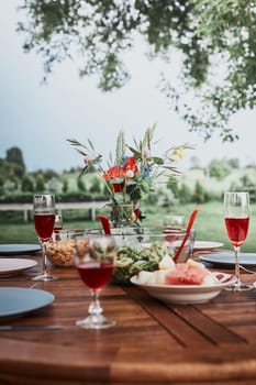 Dinner in an apple orchard garden on wooden table with salads and wine decorated with flowers. Close up of table with food prepared for family dinner