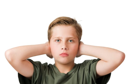 Head and shoulders frontal view of a young male teenage boy in front of a white background covering his ears with his elbows raised and looking seriously at the camera.