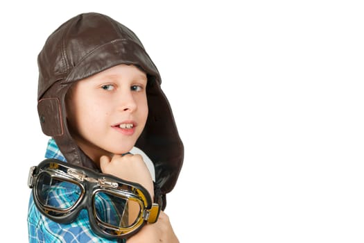 Side head and shoulder view of a 10-year-old Caucasian boy wearing a leather cap and wearing stylish motorcycle goggles over his shoulder against a white background and looking cheekily into the camera.
