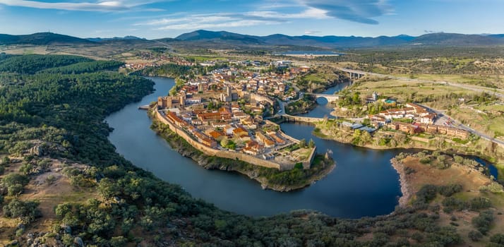 Aerial view of Buitrago del Lozoya, a well preserved historic village near Madrid, surrounded by the Lozoya river, with the Guadarrama mountain chain and reservoir in the background.