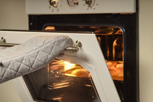 Female hands in mittens open oven door to check the bakery products