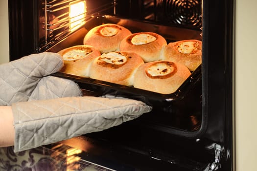 Female hands in mittens take bakery products off the oven