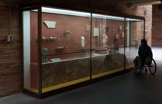Merida, Spain - May 23th, 2021: Woman in a wheelchair iobserves glass cabinet at National Museum of Roman Art in Merida, Spain