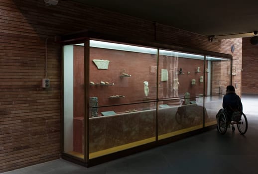 Merida, Spain - May 23th, 2021: Woman in a wheelchair iobserves glass cabinet at National Museum of Roman Art in Merida, Spain