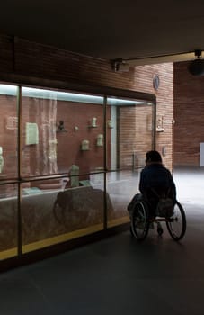 Merida, Spain - May 23th, 2021: Woman in a wheelchair iobserves glass cabinet at National Museum of Roman Art in Merida, Spain