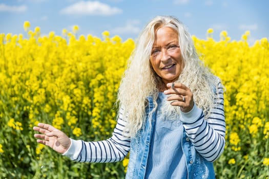 Elderly Woman smoke a cigarette in rape field with yellow blossums
