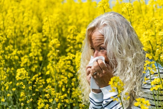 Woman suffers from allergy in a rape field and has to sneeze.